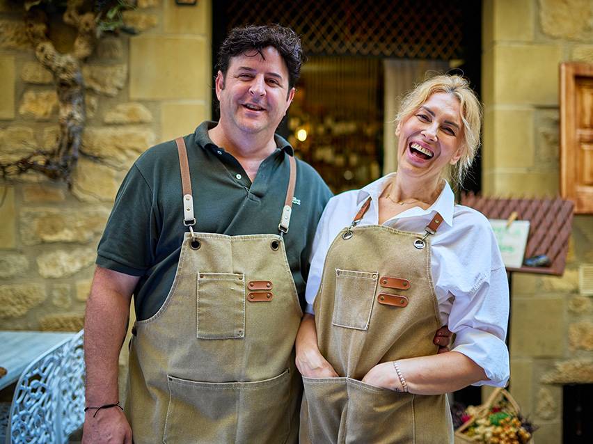 Man and woman in canvas aprons, smiling in front of a shop.