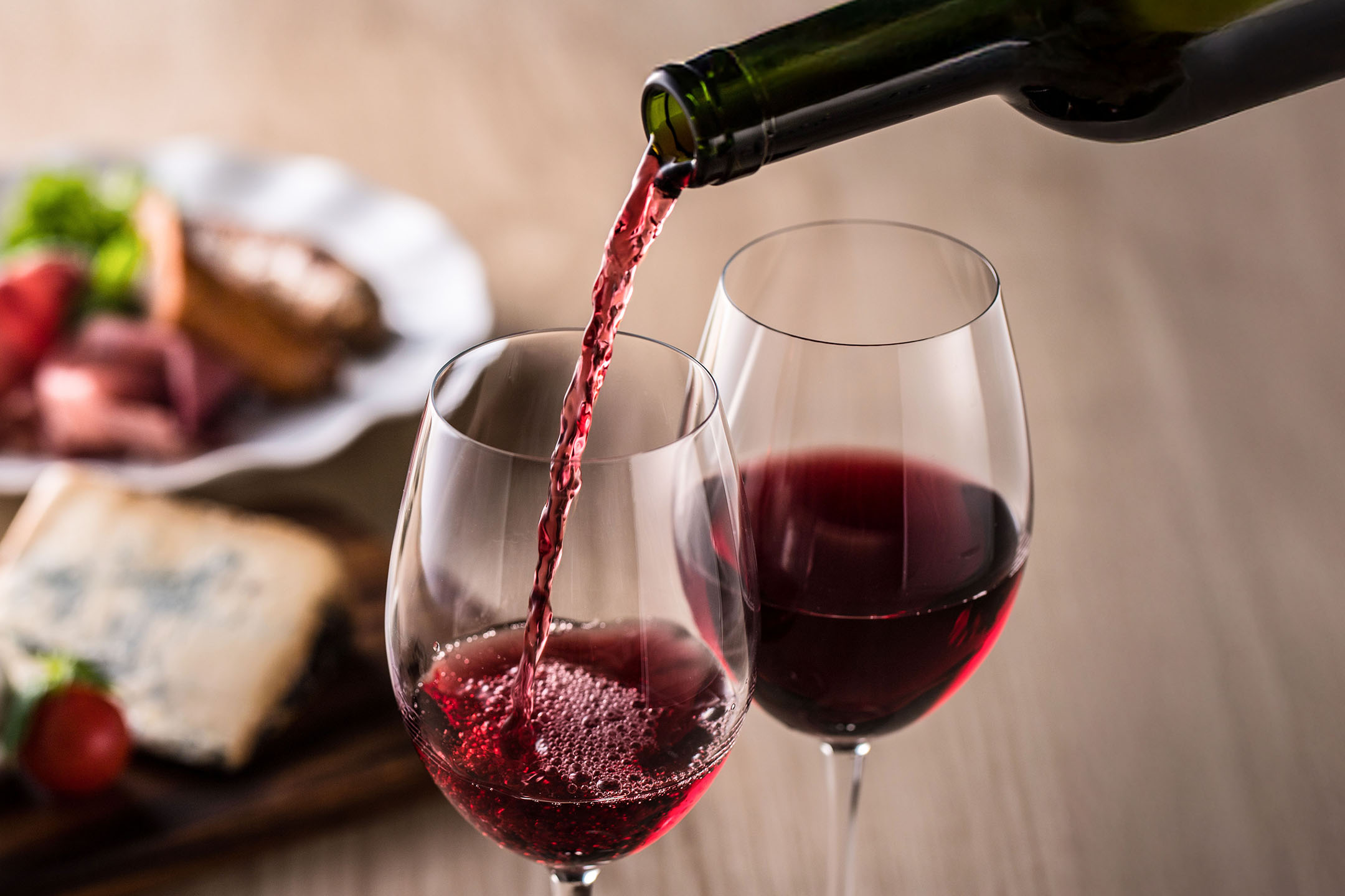 Red wine being poured into a glass, with appetizers in the background.