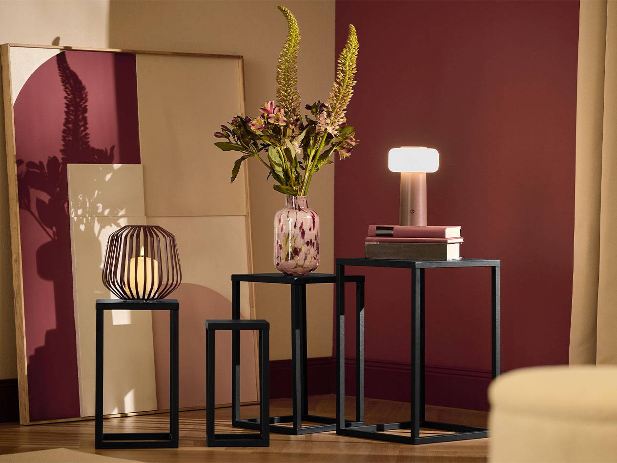 Three black side tables with a candle, a vase of flowers, and a lamp.