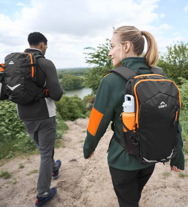 Two hikers on a trail, one carrying a Crivit backpack and an orange water bottle.