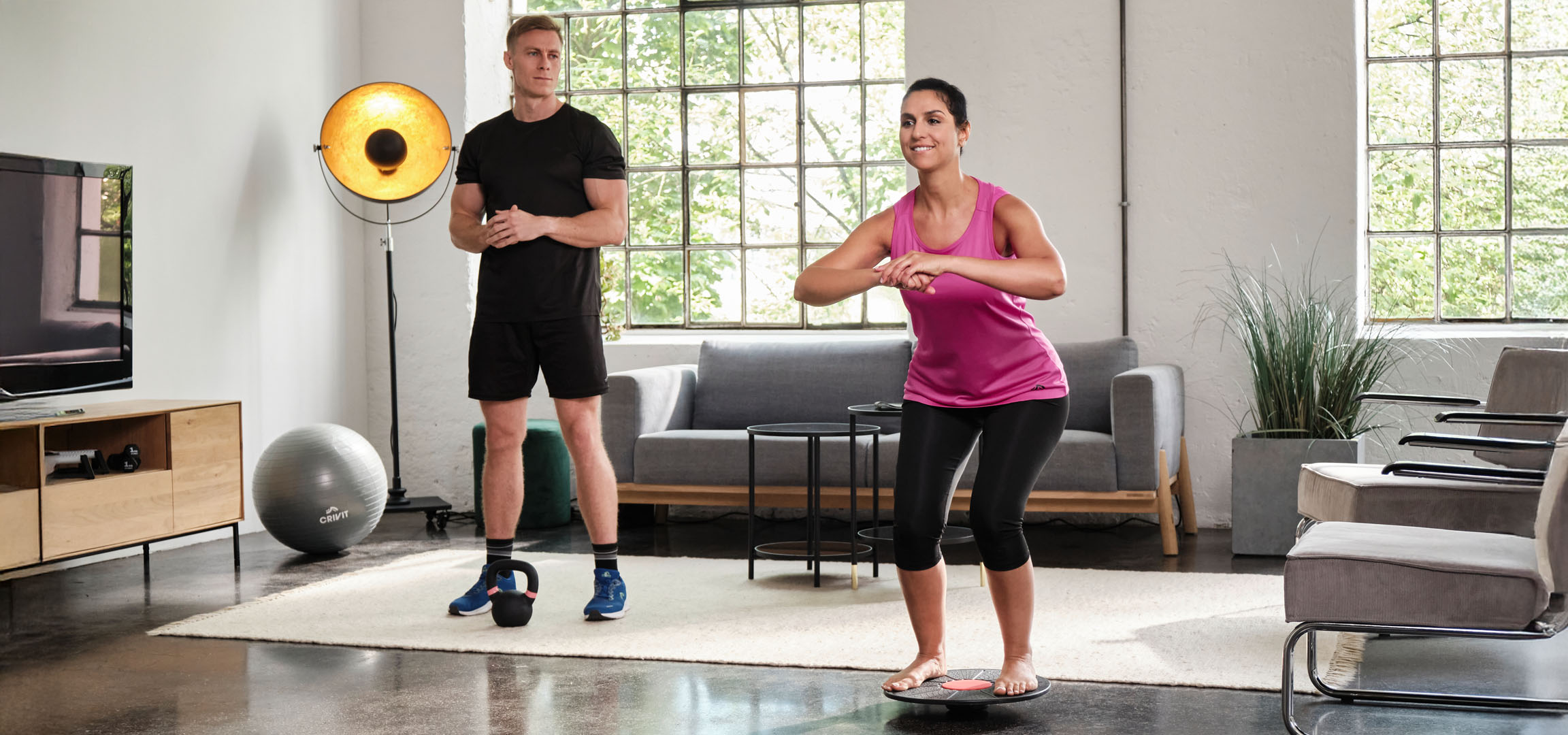 Woman and man exercising at home with balance board and kettlebell.