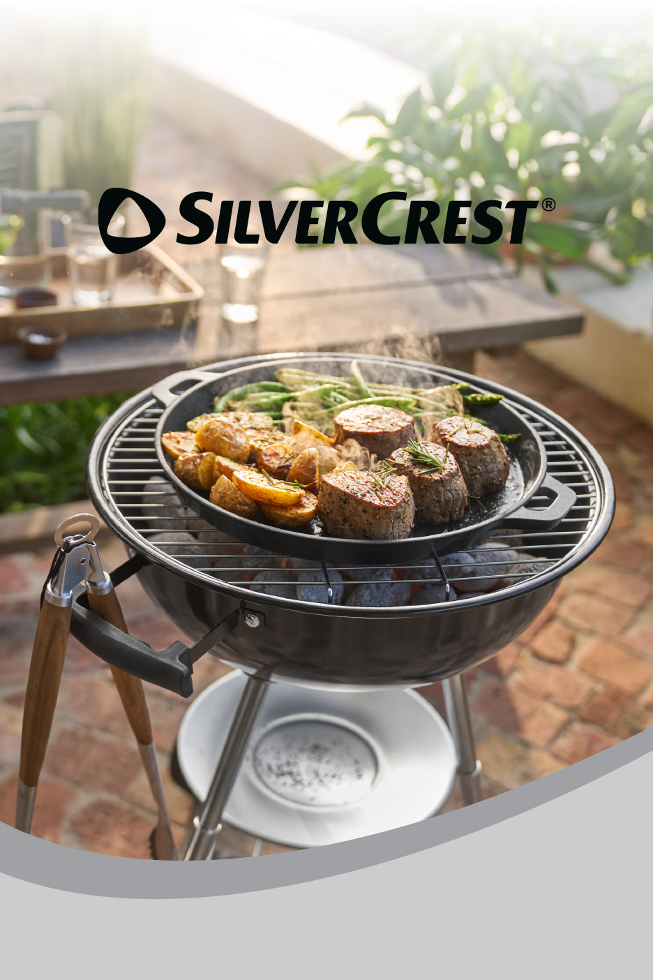 Charcoal grill with a cast iron pan cooking meat and vegetables, SilverCrest logo above.