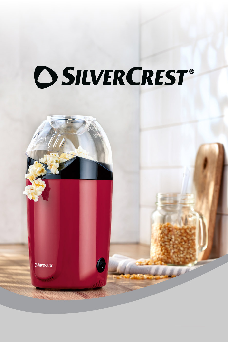 Red popcorn maker with popcorn spilling out, next to a jar of kernels on a wooden counter.