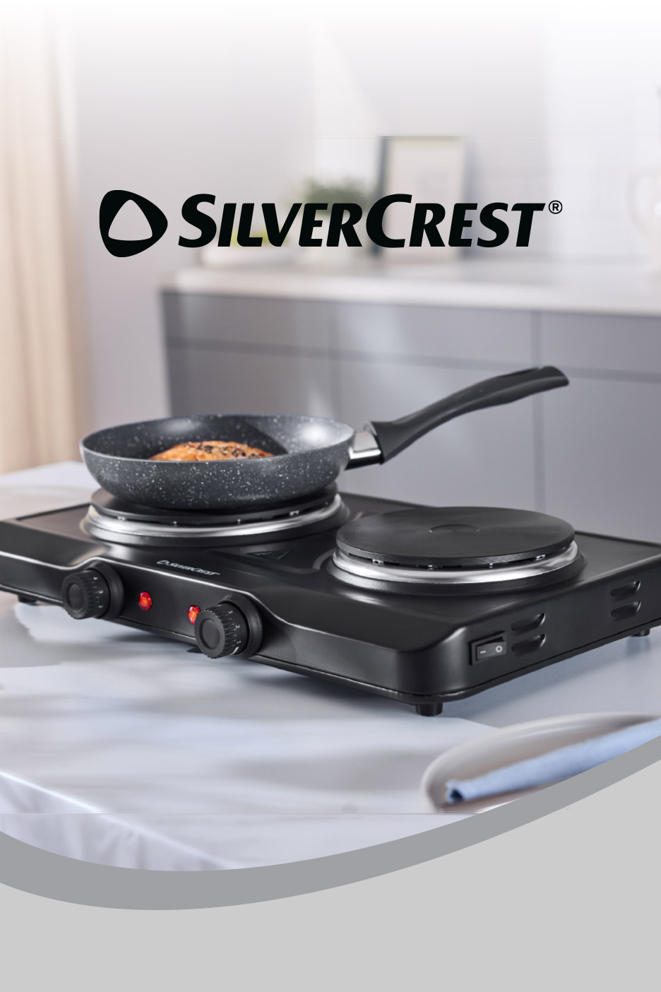 Portable double hot plate with a frying pan cooking food, set on a white tablecloth.