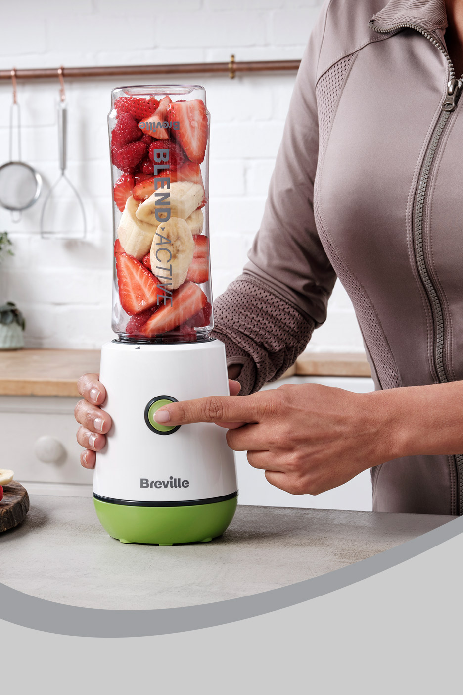 Person blending strawberries and bananas in a white and green personal blender.