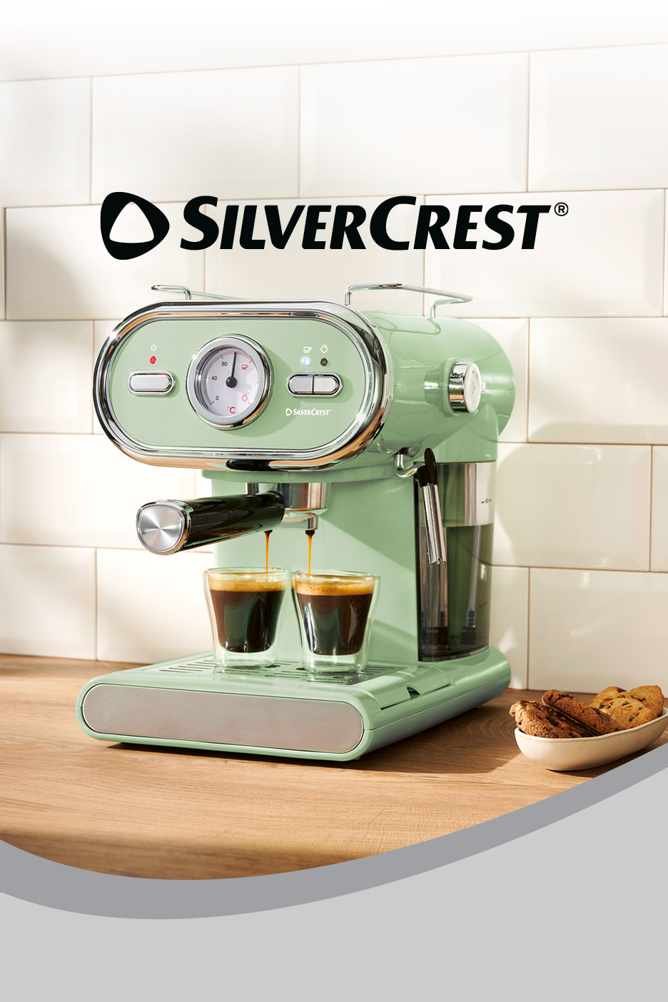 A retro-style mint green espresso machine brewing coffee into two glasses on a wooden counter.