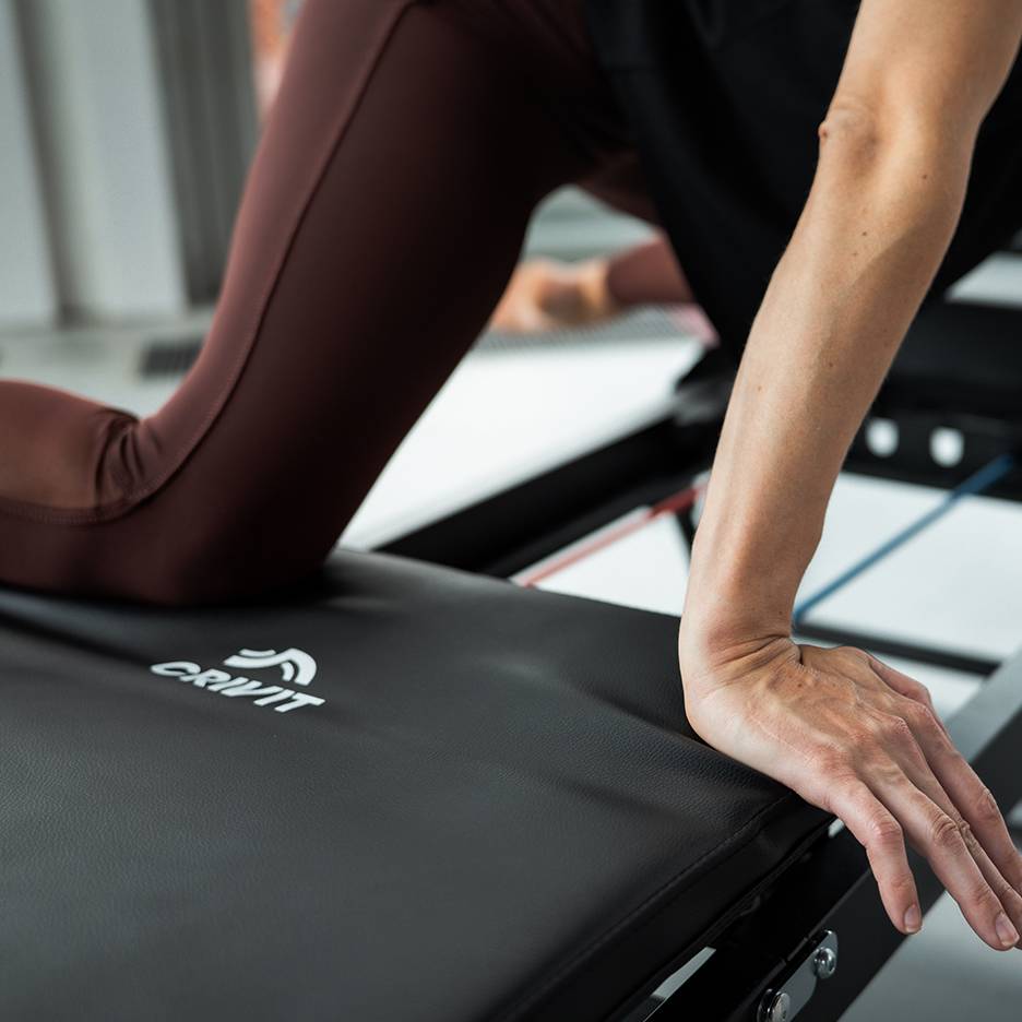 Woman exercising on a Crivit fitness machine in brown yoga pants.