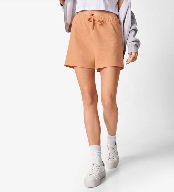 A woman models a pair of light orange drawstring shorts and white platform sneakers.