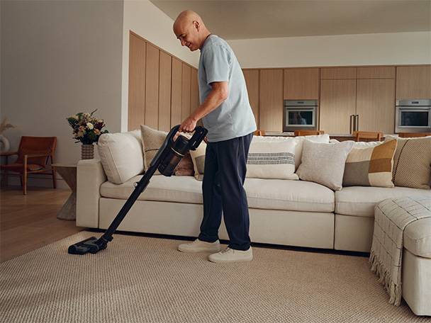 Man vacuuming a living room with a cordless stick vacuum cleaner.