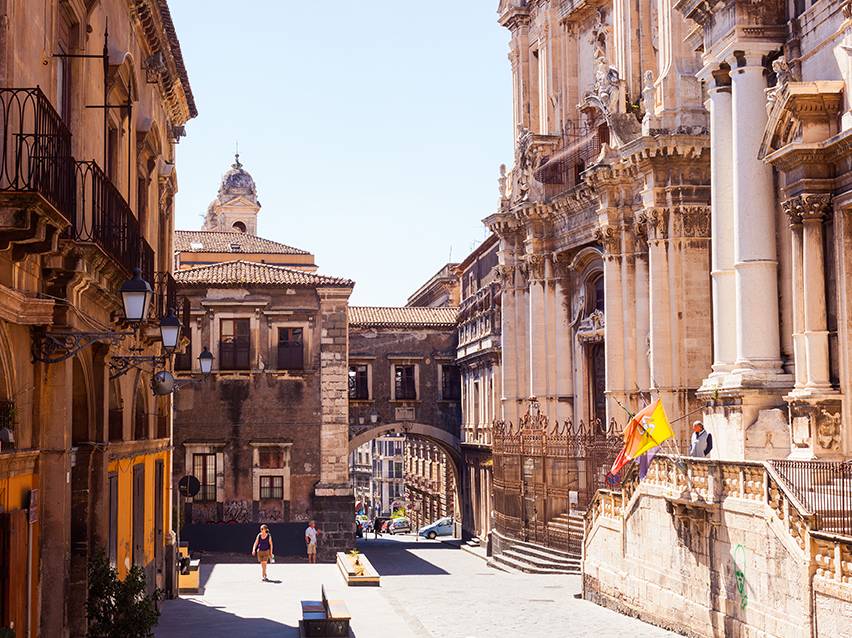 Sunny historic street with old buildings and passersby.