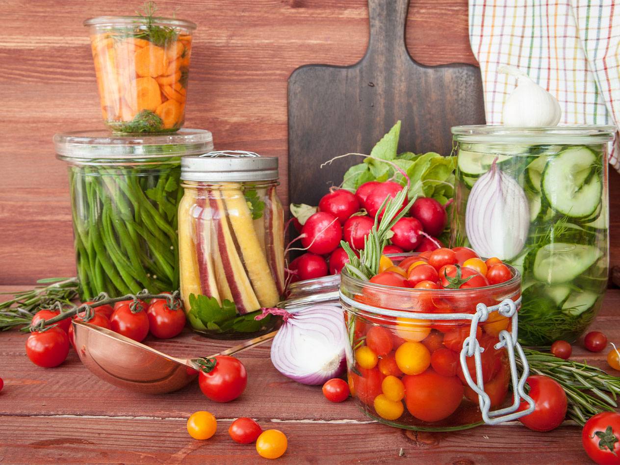 Various pickled vegetables in glass jars, including carrots, green beans, and tomatoes.