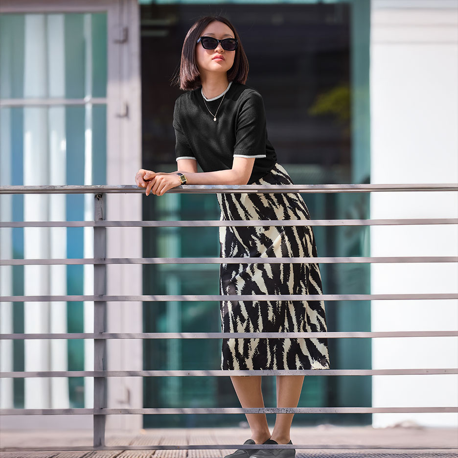 Woman in a black top and zebra print skirt leaning on a railing.