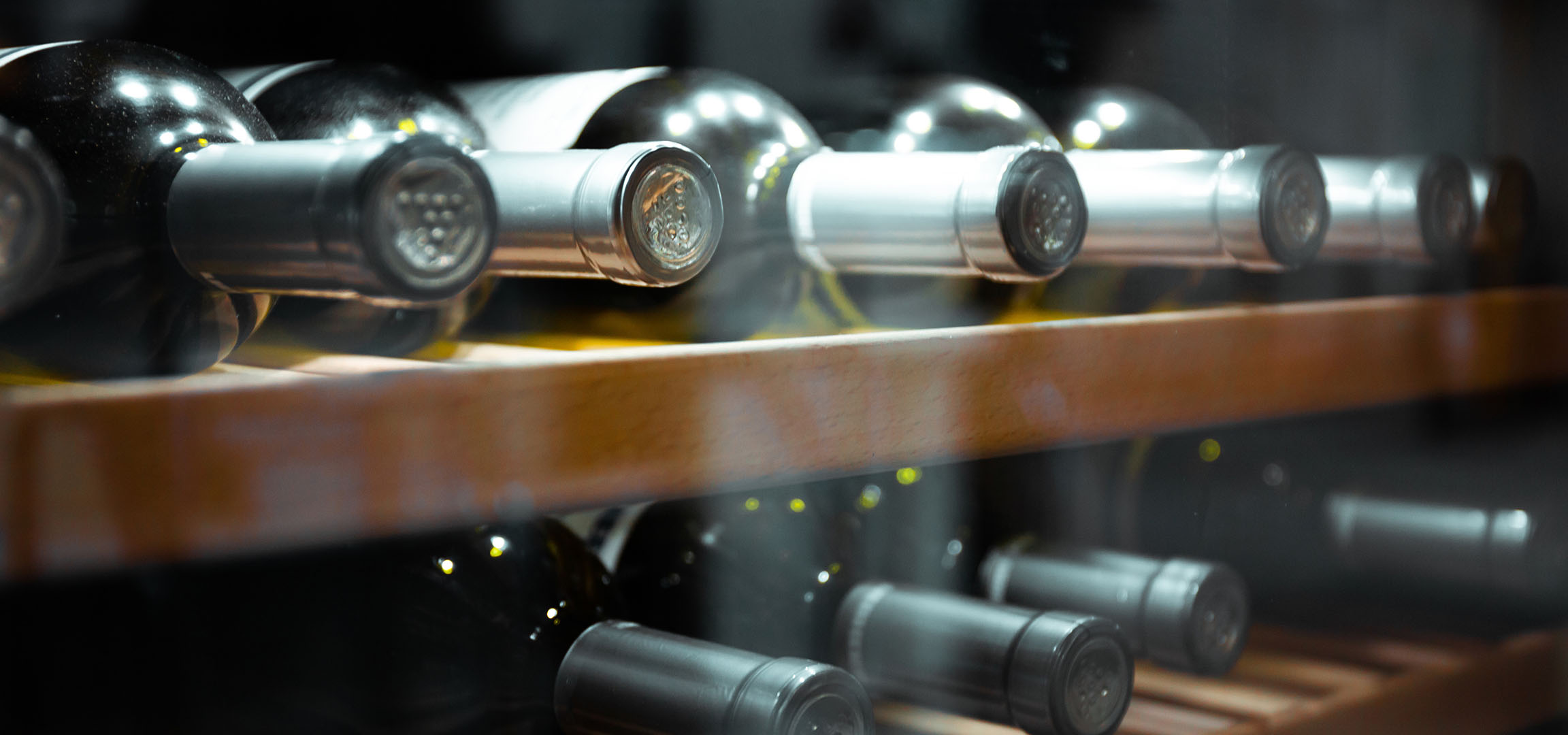 Close-up of wine bottles on a wooden shelf, showcasing their caps and reflections.