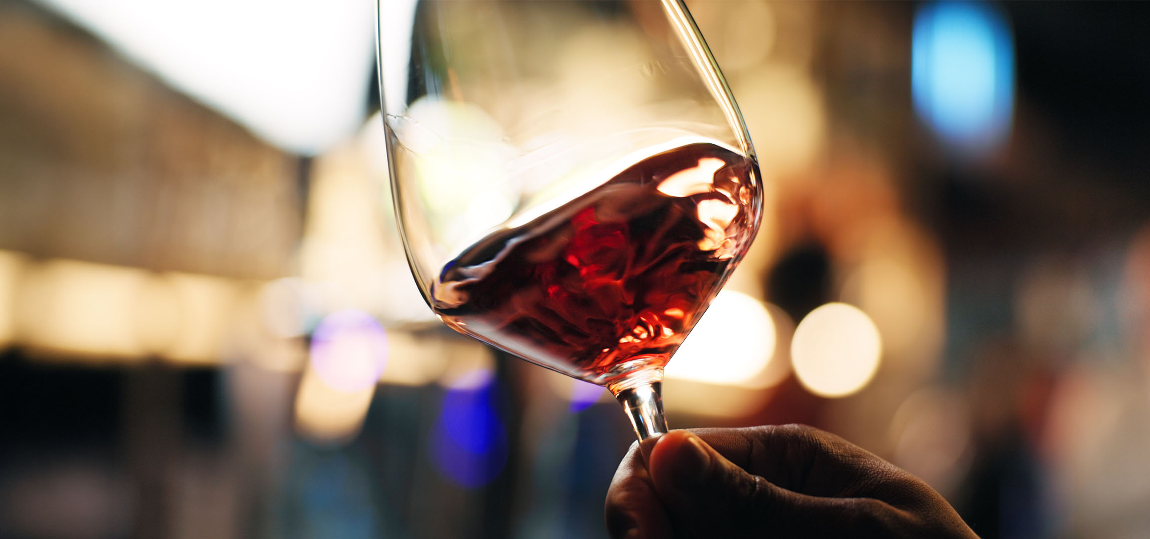 Close-up of a glass of red wine with blurred lights in the background.