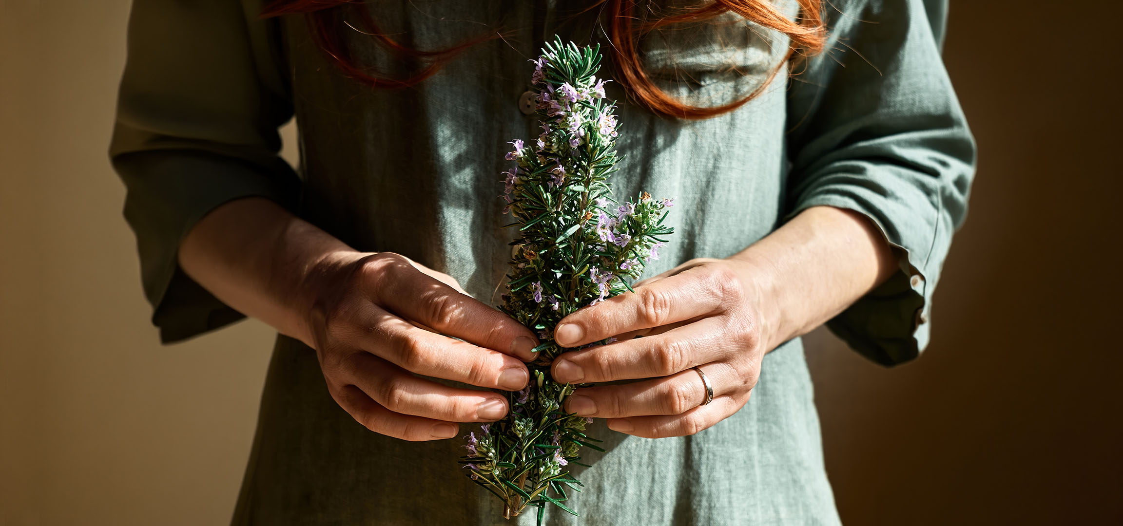 Woman in green dress holding flowering rosemary.