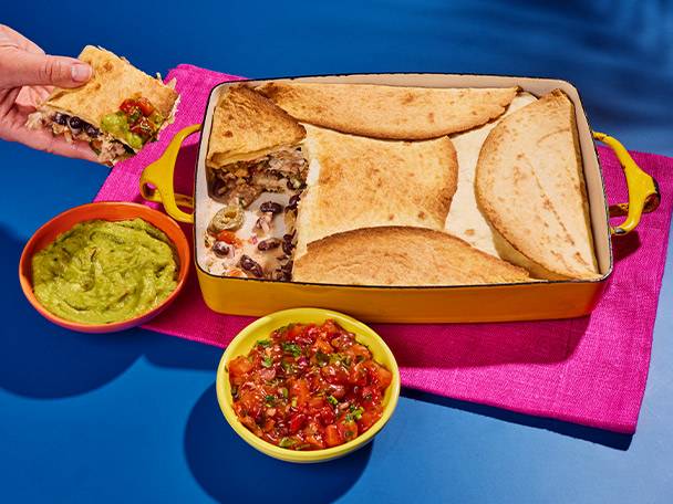 Quesadillas in a yellow baking dish, with guacamole and salsa on a blue background.