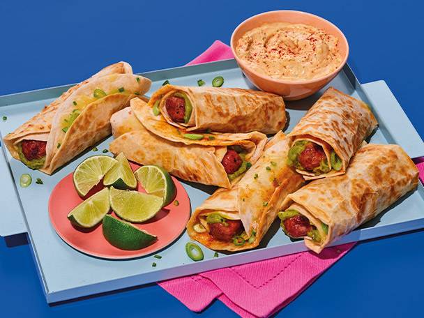Tray of meatball wraps with guacamole, lime wedges, and a bowl of hummus.