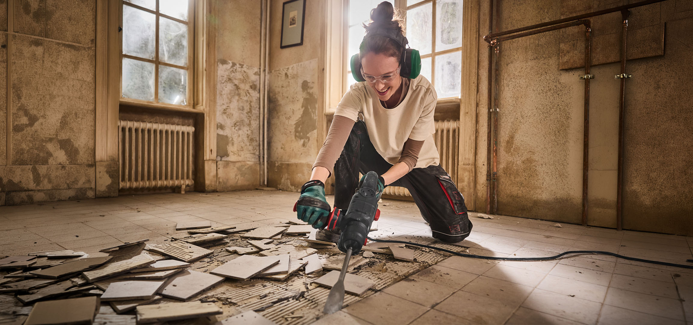 Woman using a demolition hammer to remove floor tiles in an old room