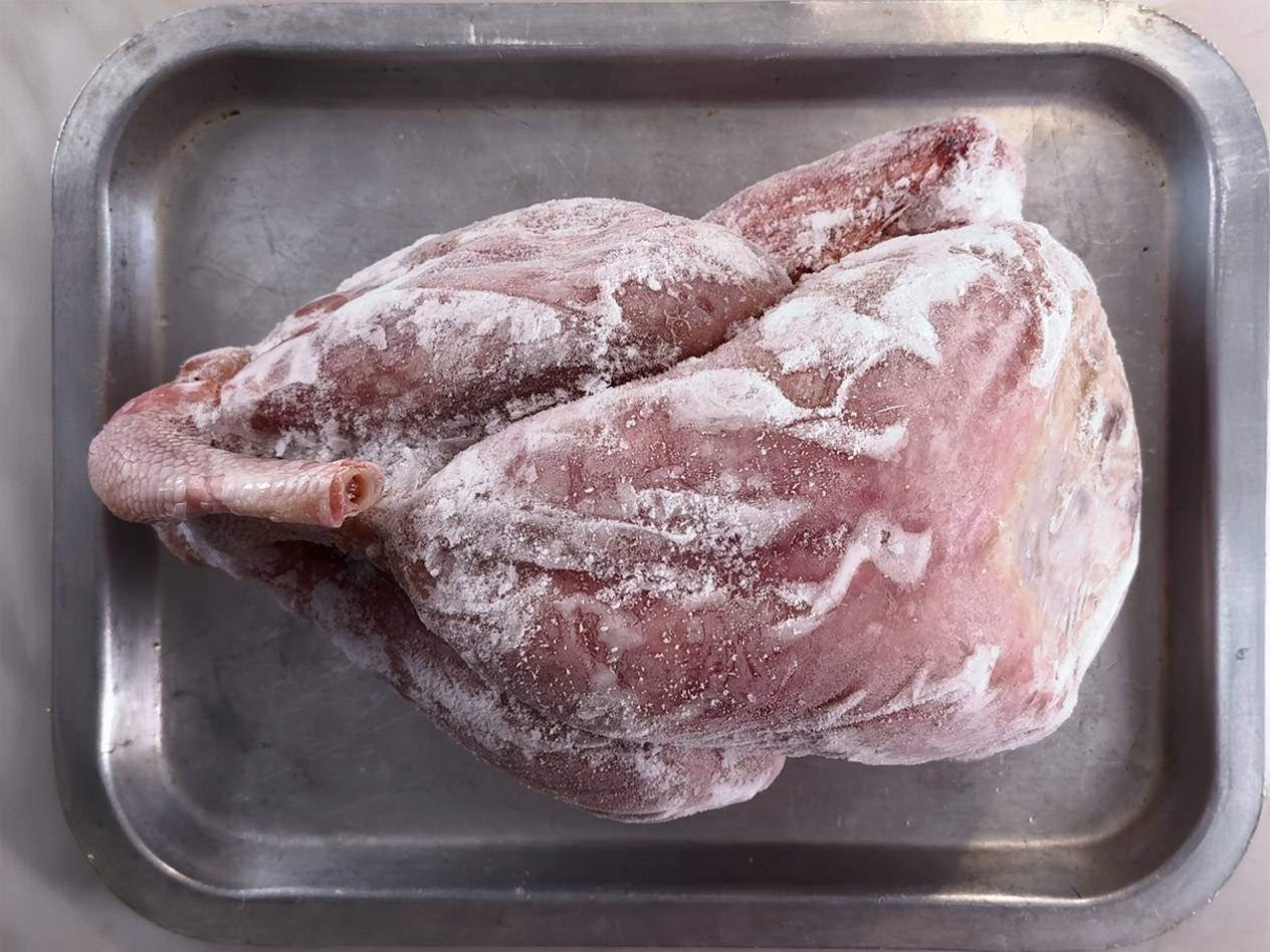 Frozen whole chicken on a metal tray, covered in ice crystals.