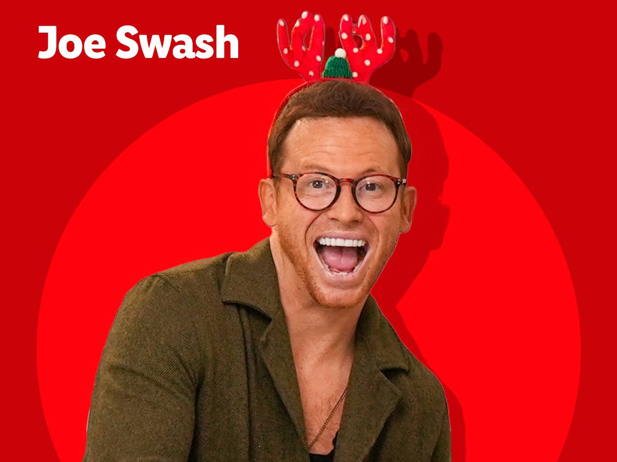 Joe Swash wearing festive reindeer antlers on a red background.