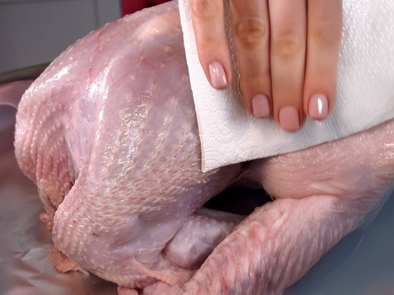 A person drying a raw turkey with a paper towel.