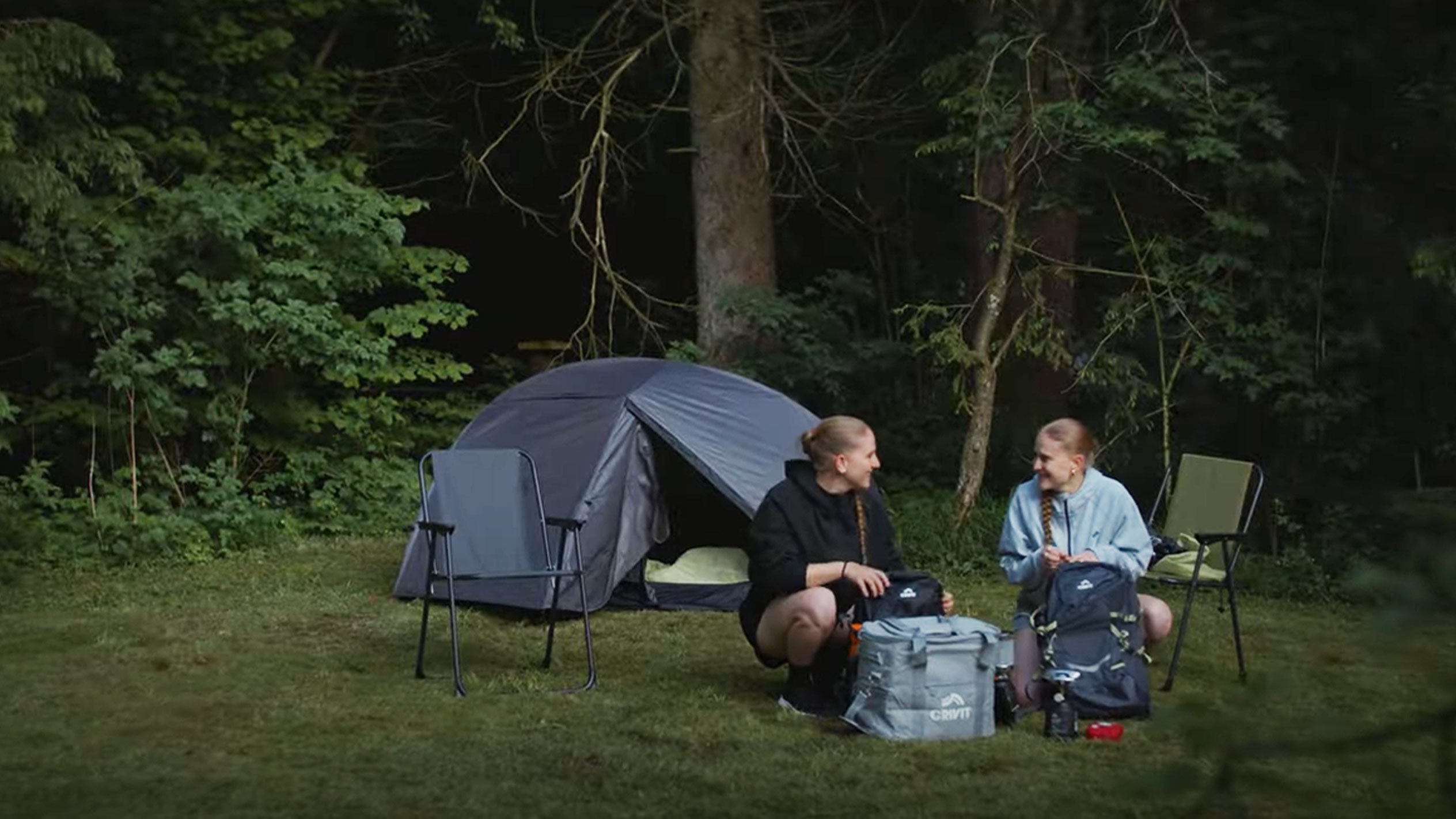 Two women camping with a Crivit tent and folding chairs.