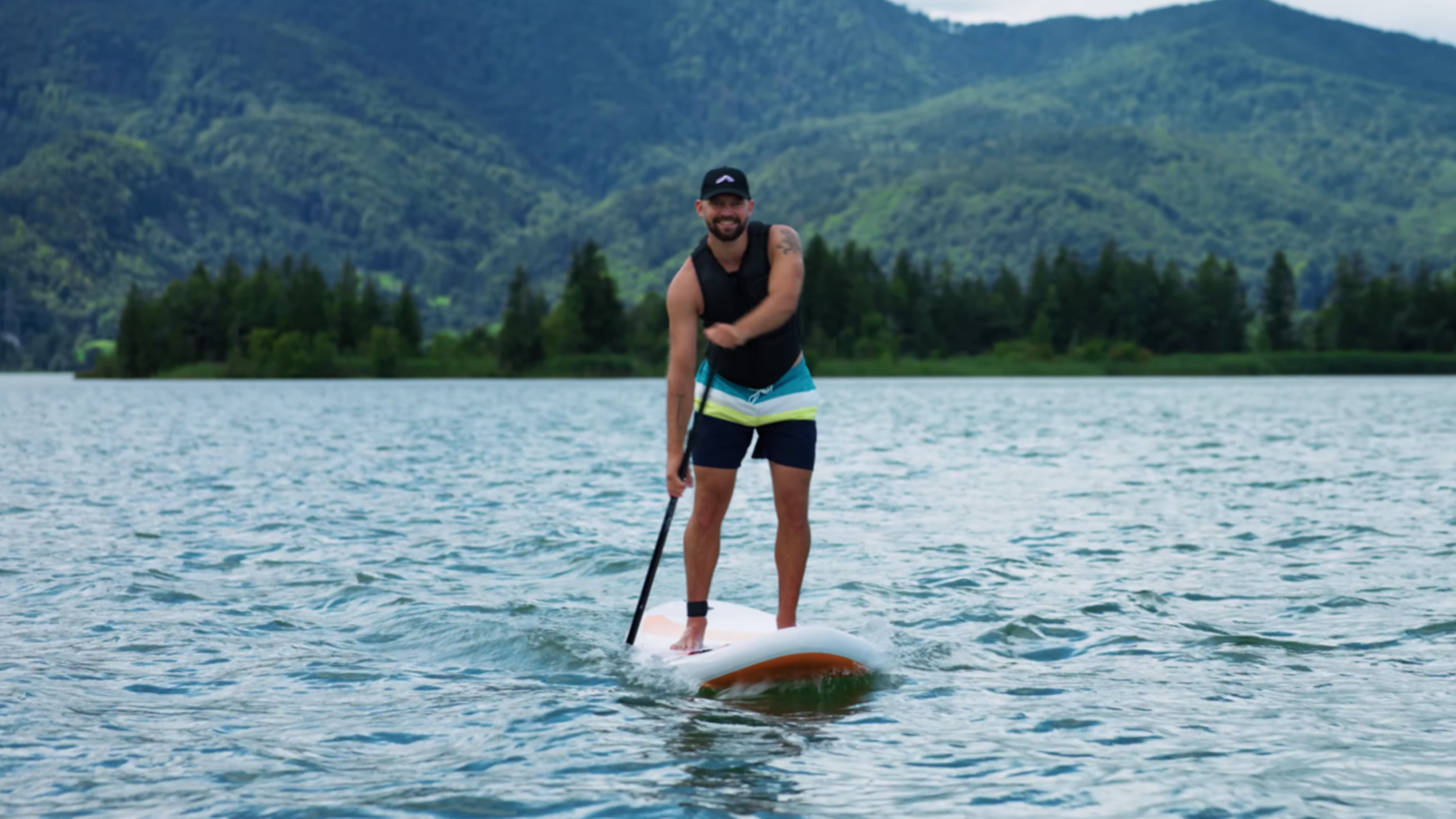 Man on a paddleboard on a lake with mountains in the background.