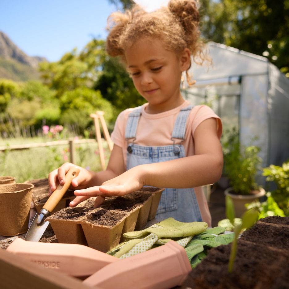 Girl planting seeds in peat pots with gardening tools and gloves.