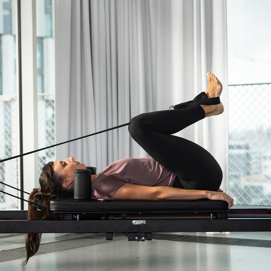 Woman exercising Pilates on a reformer with legs up.