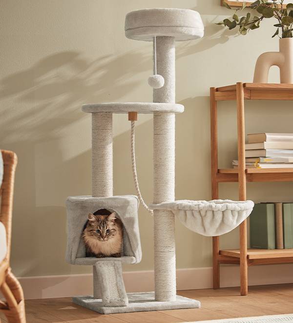 A light grey cat tree with a hanging toy and a hammock, featuring a cat resting in a cozy cubby.