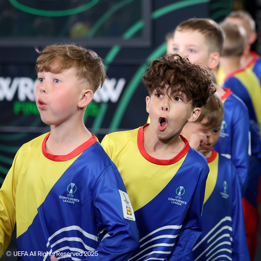 Two boys in yellow and blue football jerseys with UEFA Conference League logos.