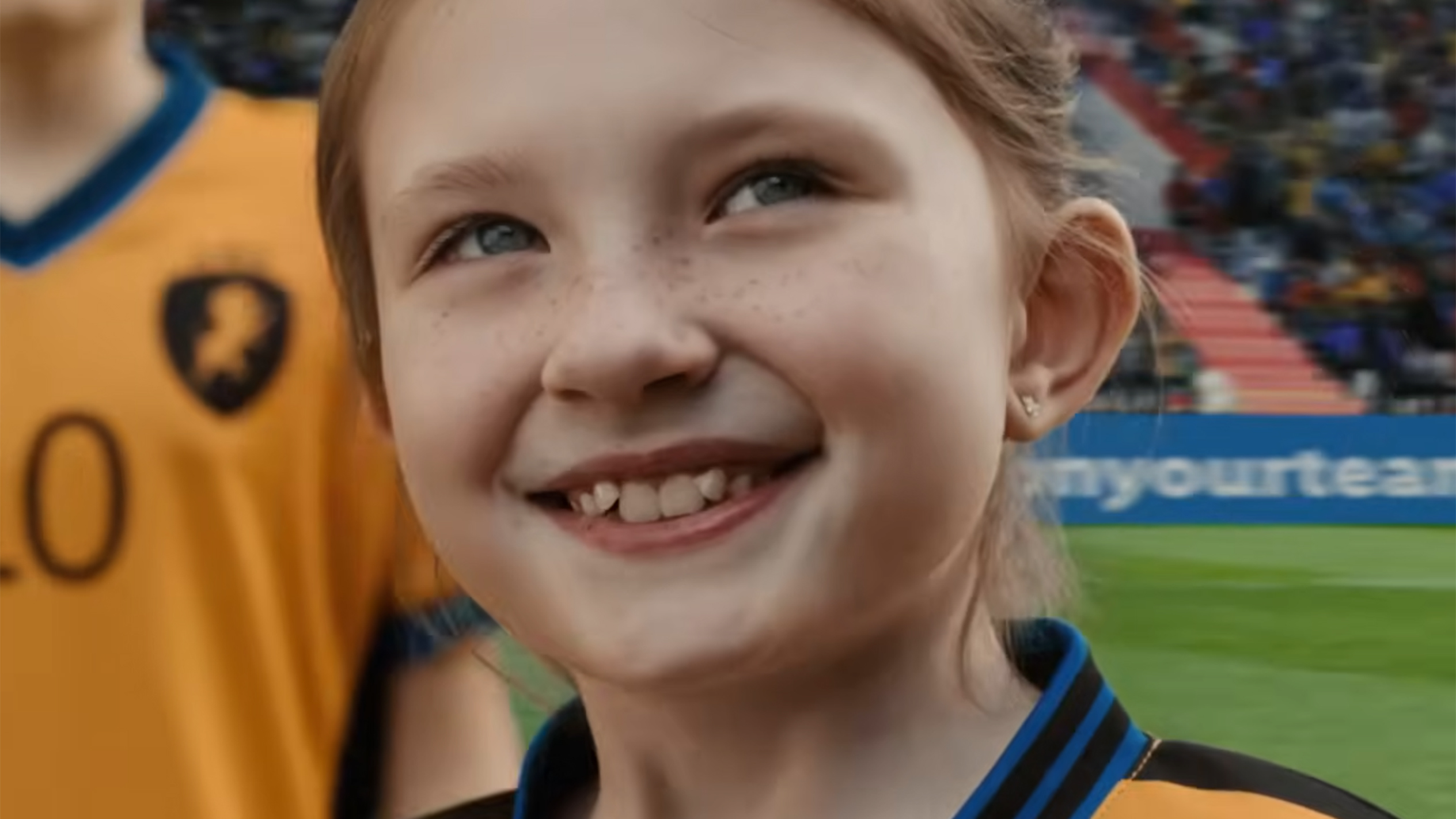 A freckled girl smiles in a soccer jersey.