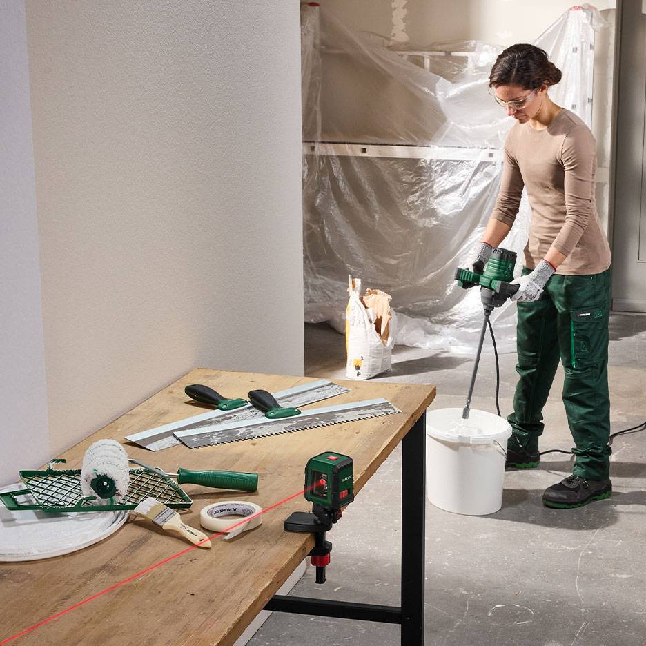 Woman mixing building material with painting and leveling tools on a table.