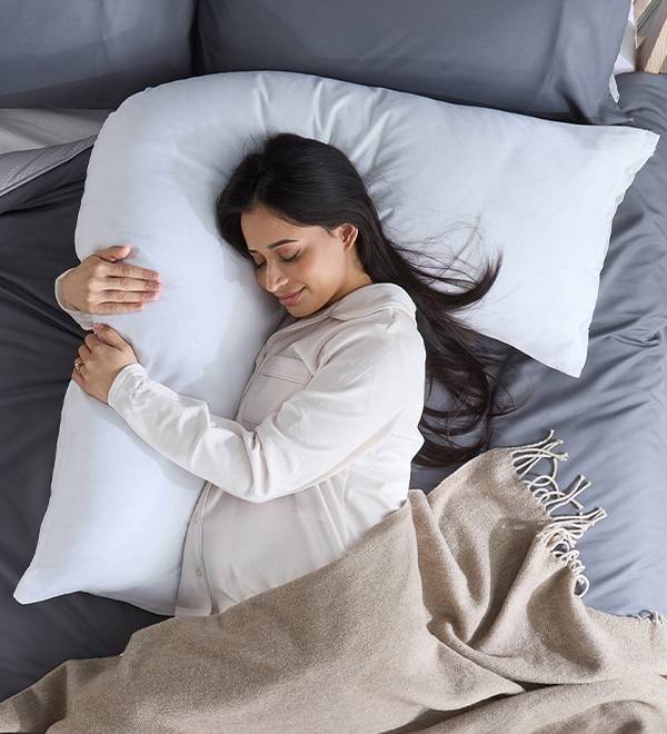 A pregnant woman sleeps comfortably on a U-shaped pregnancy pillow.