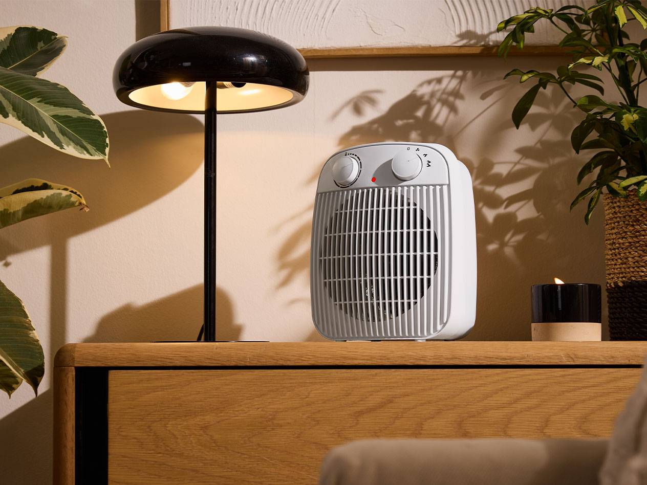 White heater and black table lamp on a wooden furniture piece in a cozy room.