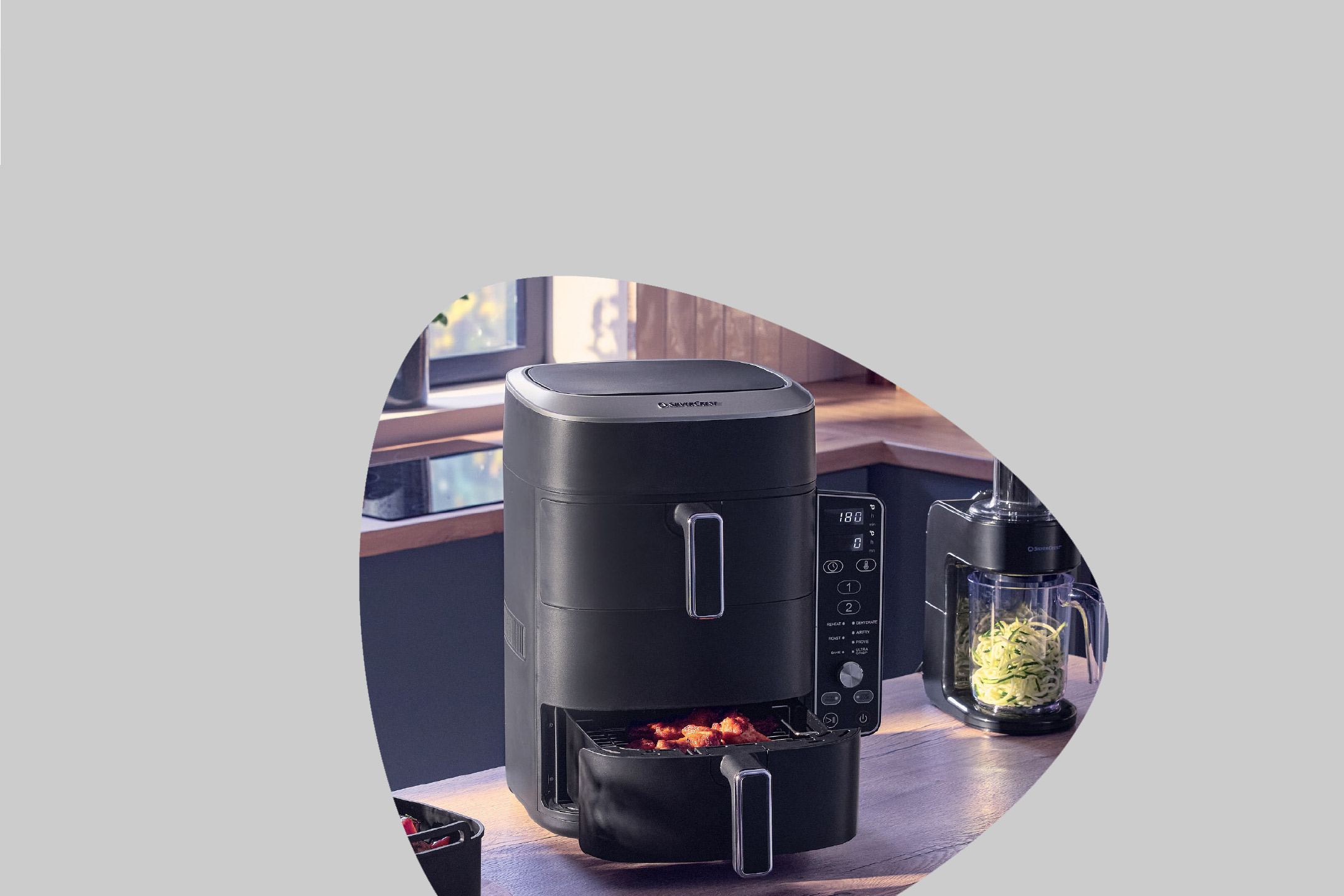 Air fryer cooking chicken wings, with a spiralizer next to it, in a kitchen setting.