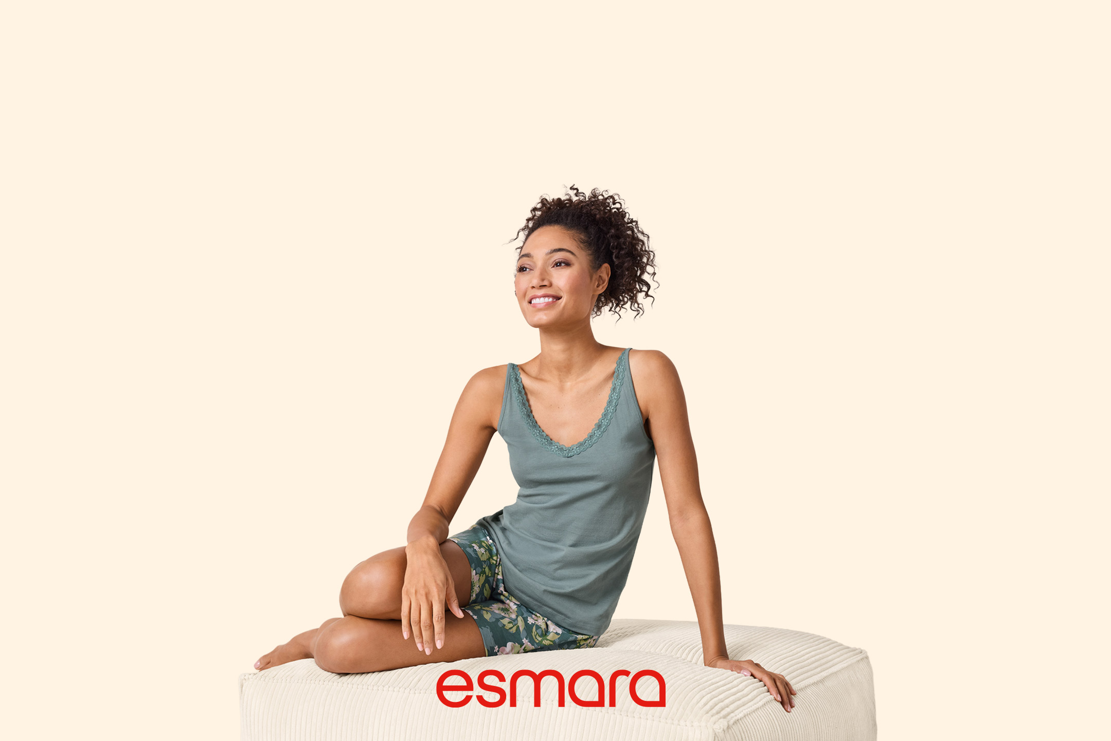 Woman in green lace-trim camisole and floral shorts, sitting on a cream ottoman.