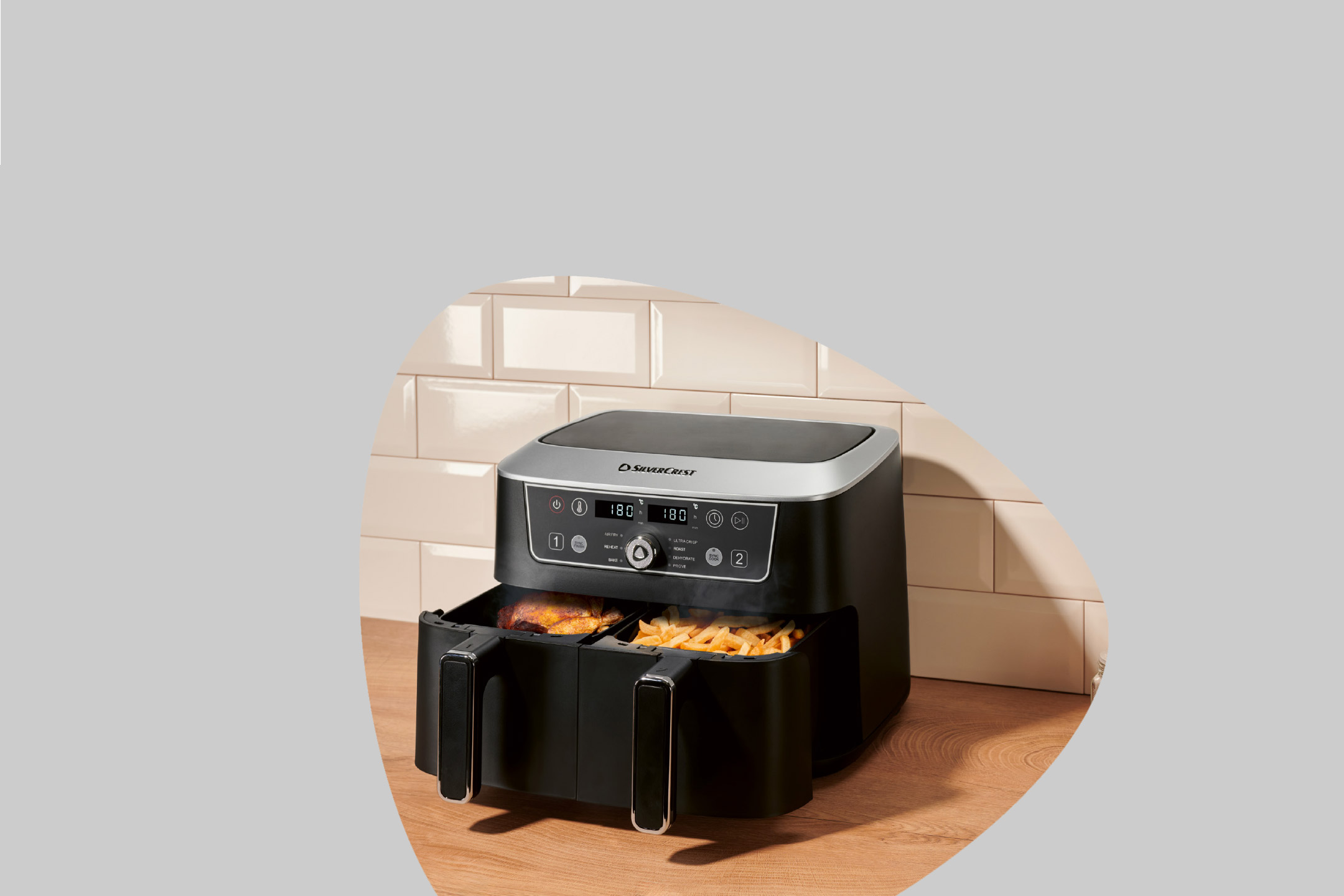 Dual-basket air fryer with chicken and fries on a wooden countertop.