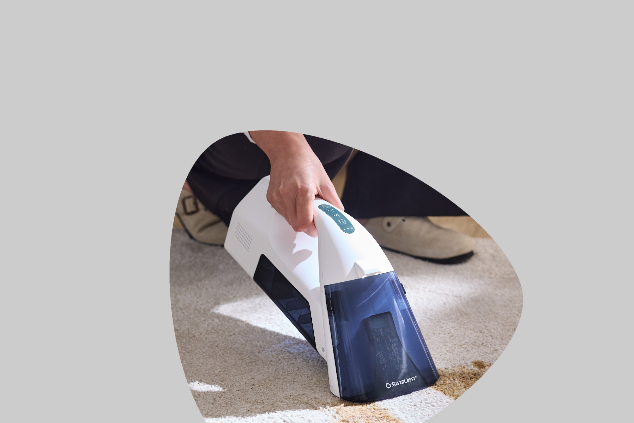 Handheld carpet cleaner removing a stain from a light-colored rug.