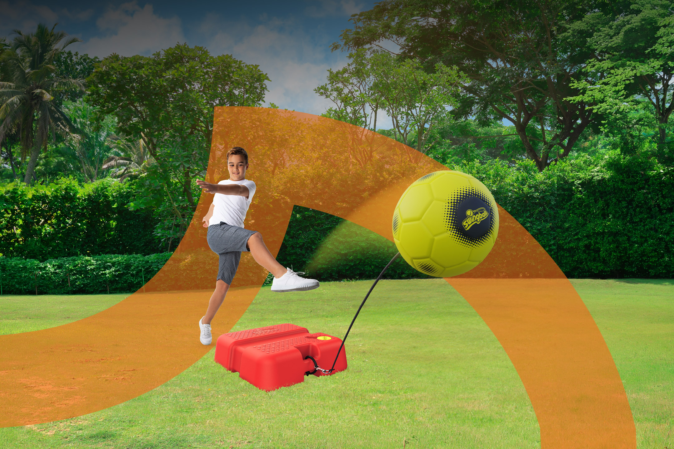 Boy kicking a tethered soccer ball on a green lawn with trees in the background.