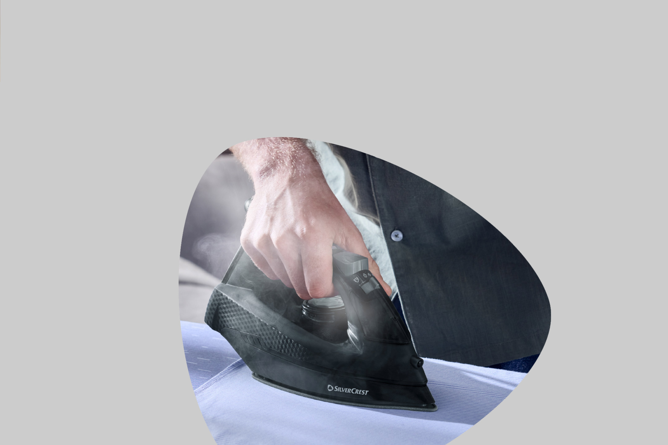 A person's hand ironing a light blue shirt with a black steam iron.
