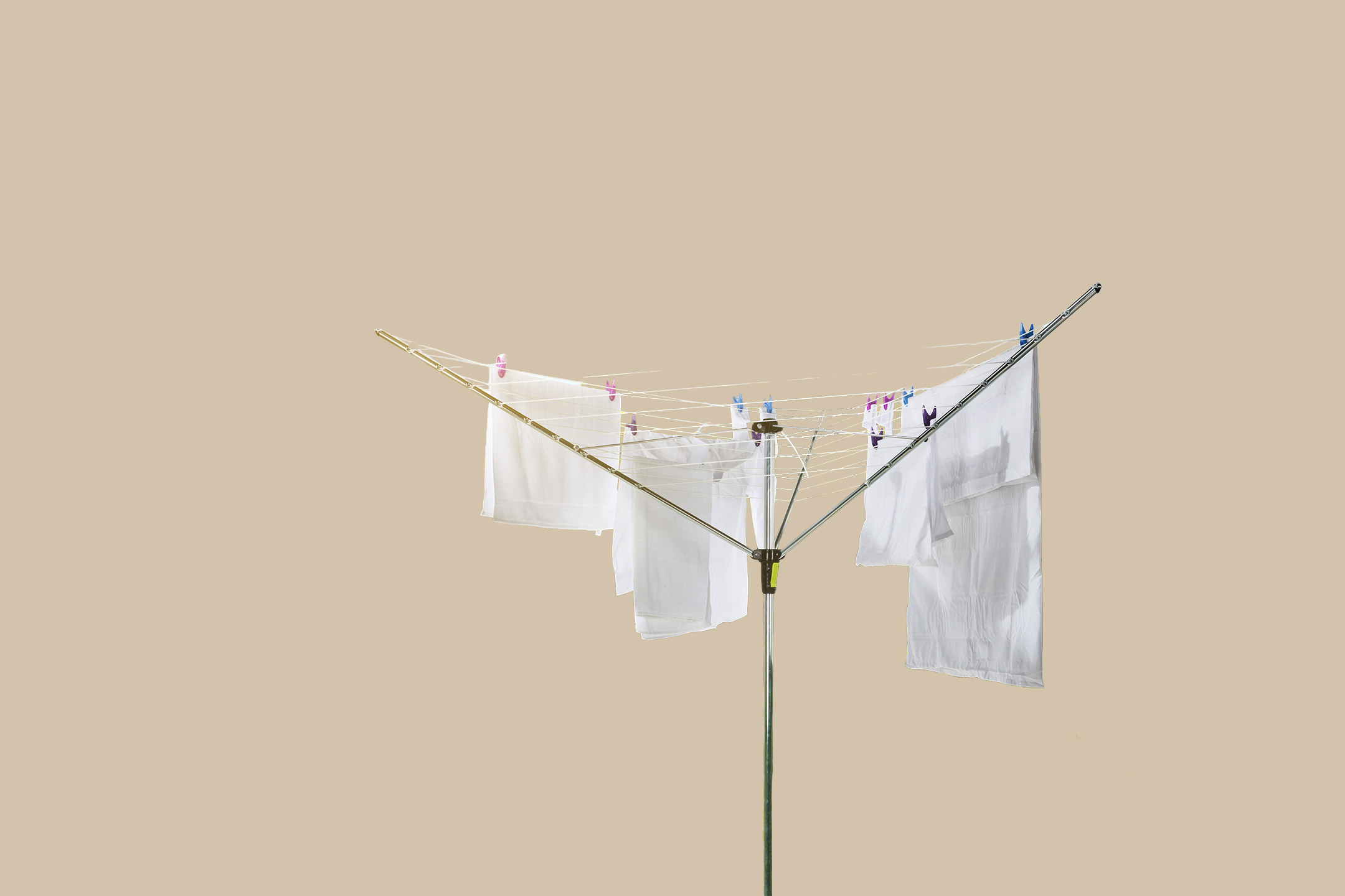 White laundry drying on a rotary clothesline with colorful pegs against a beige background.