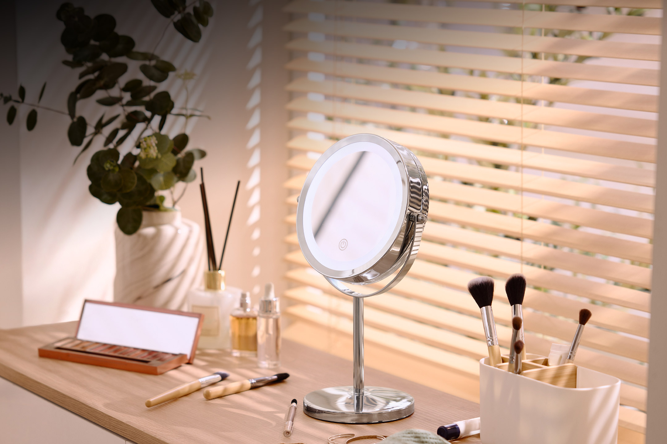 A vanity mirror with LED lighting on a wooden desk with makeup and brushes.