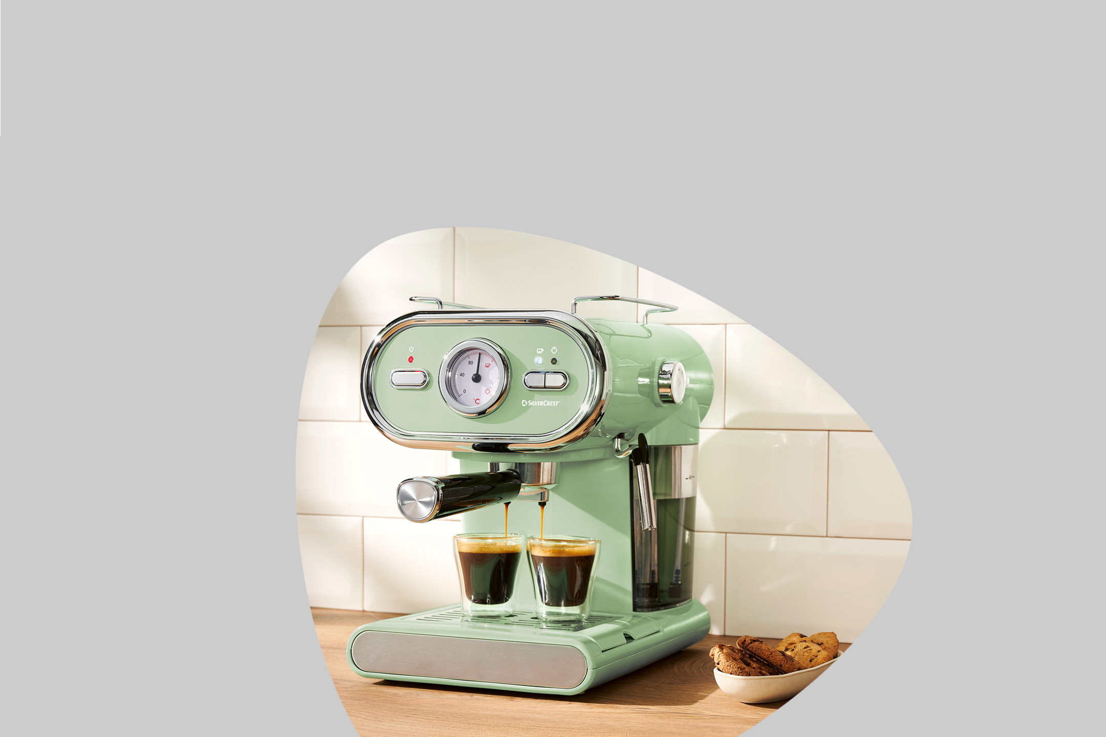 Retro-style espresso machine brewing coffee into two glasses on a wooden counter with cookies.