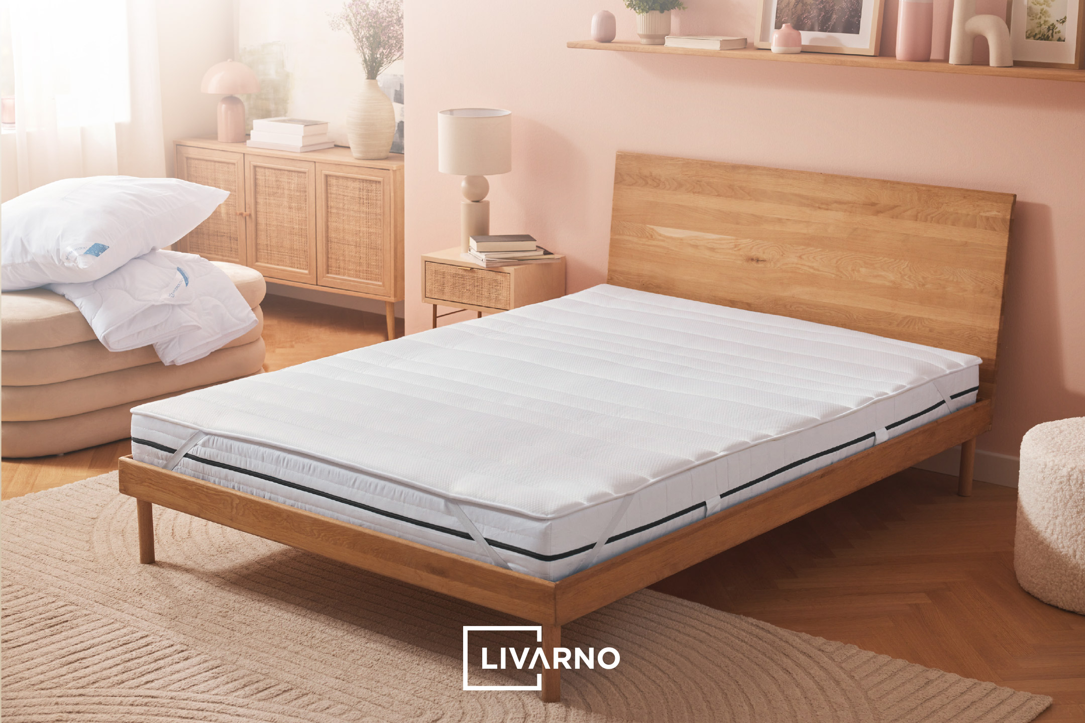 Bedroom with wooden bed frame, white mattress, pillows, duvet, and light-colored furniture.