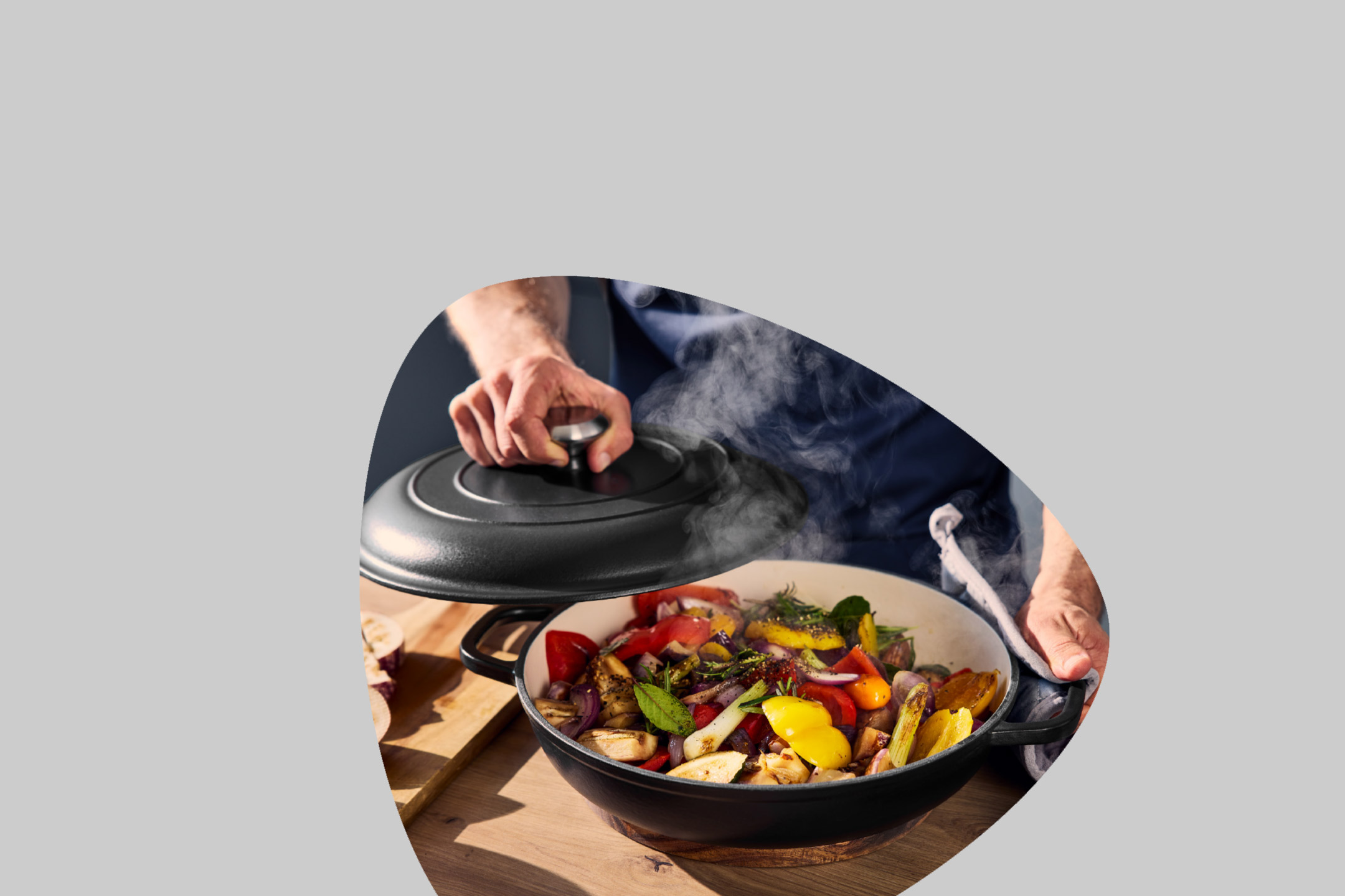 Person cooking colorful vegetables in a black cast iron pot, steam rising.