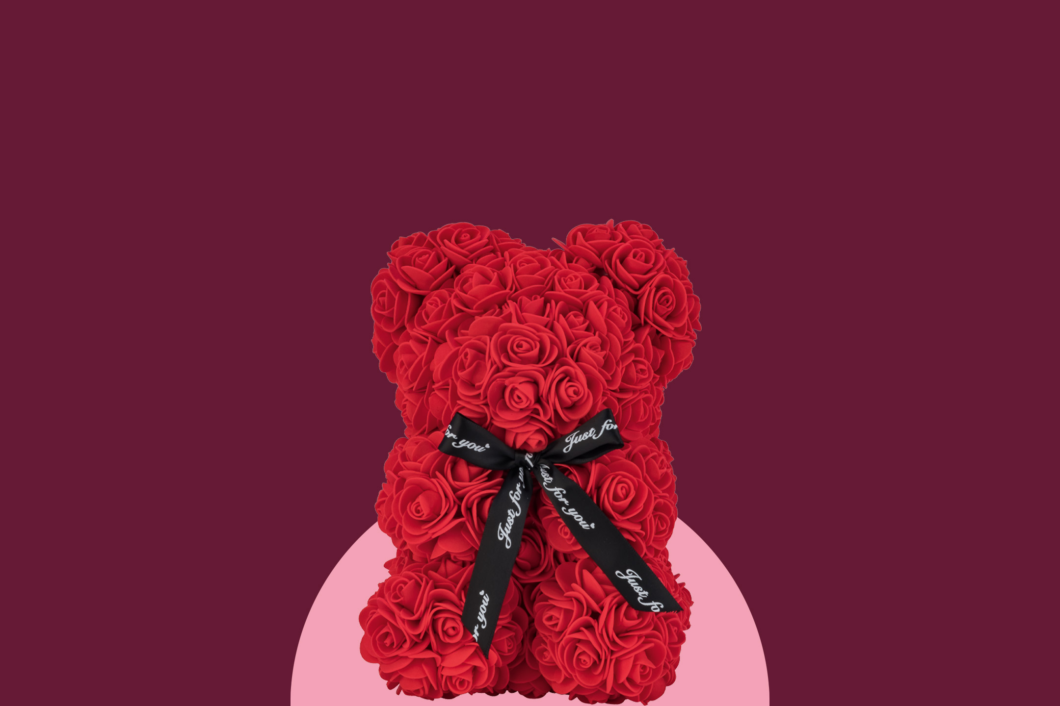 Red rose teddy bear with a black ribbon that says 'Just for you' on a two-tone pink and maroon background.