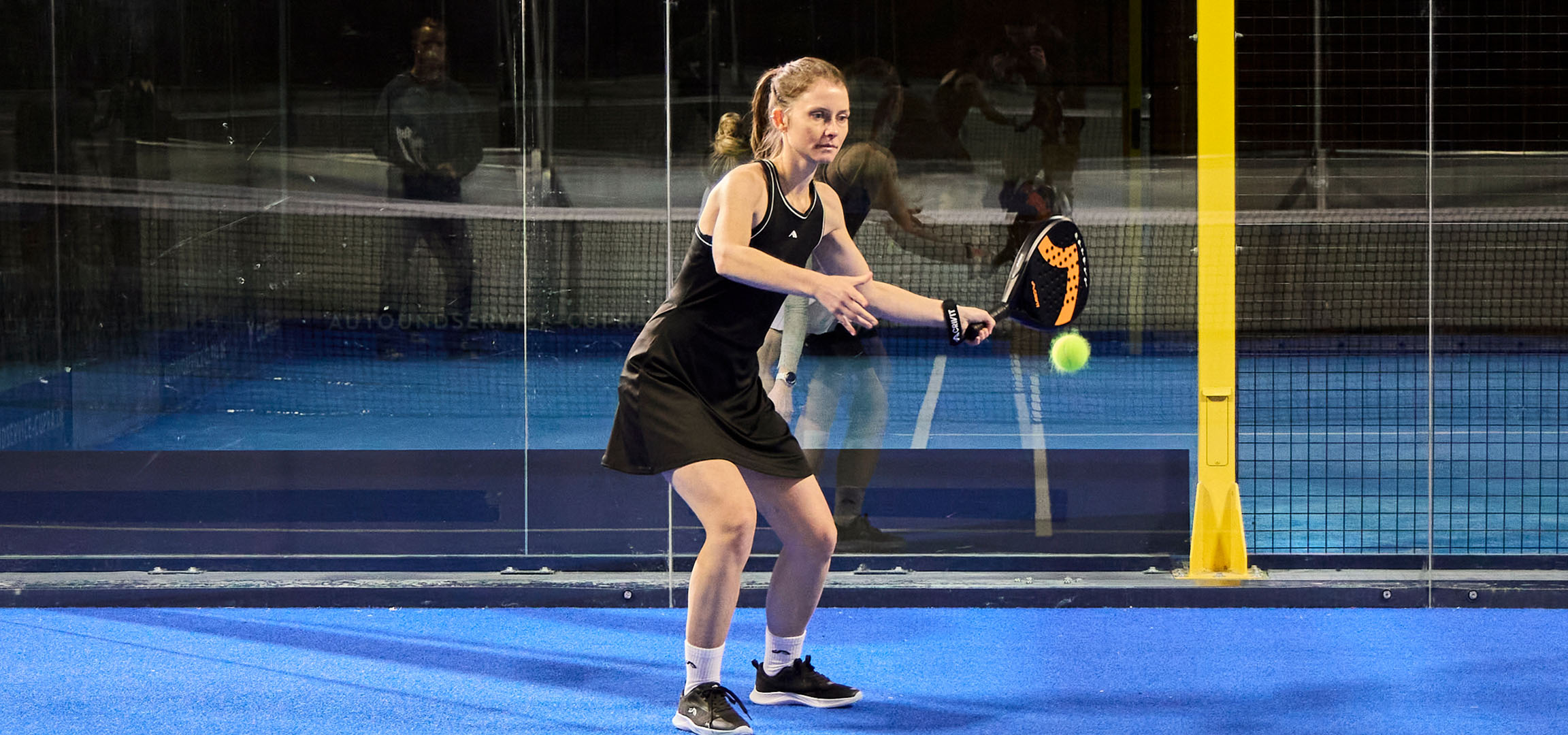 Woman playing padel on a blue court, dressed in black sportswear.