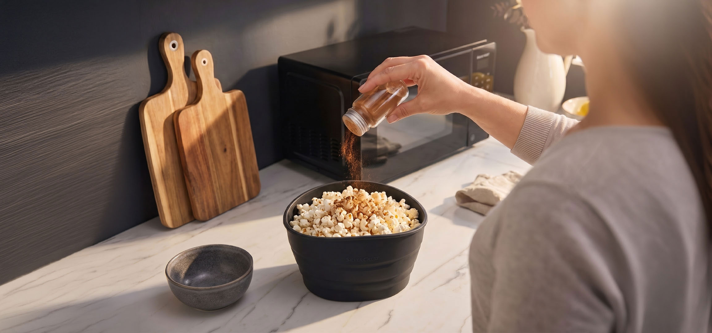 aiLabeling.aiLabelForImageAltText: Popcorn in a black bowl being seasoned with spices, next to wooden cutting boards.