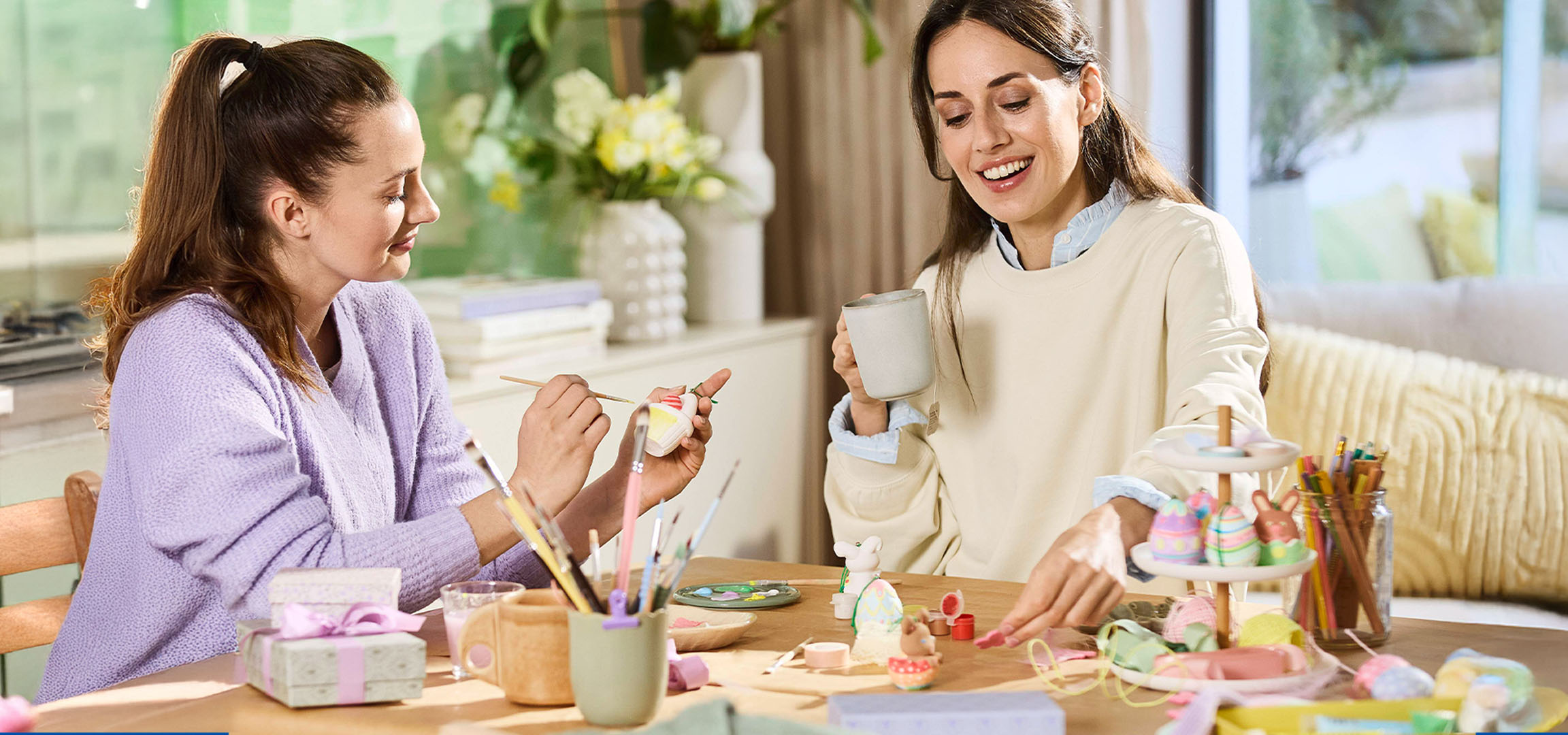 Two women decorating Easter eggs and figures at a table.